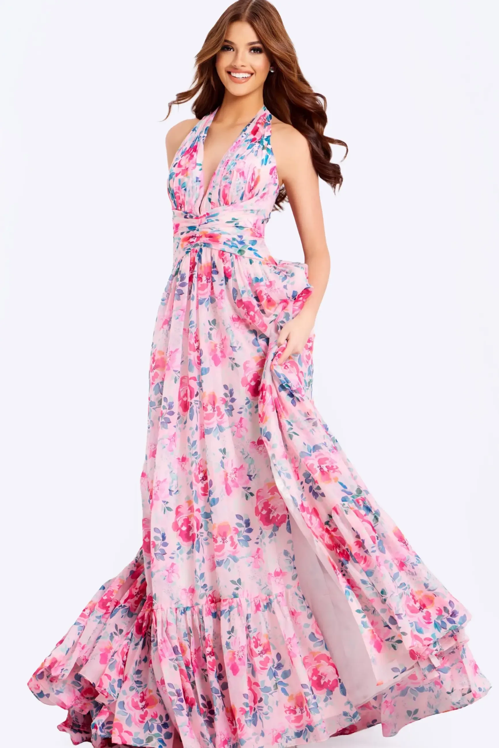 Woman in a flowing, floral pink halter dress smiles brightly. The dress features vibrant pink and purple flowers, exuding a cheerful, elegant vibe.