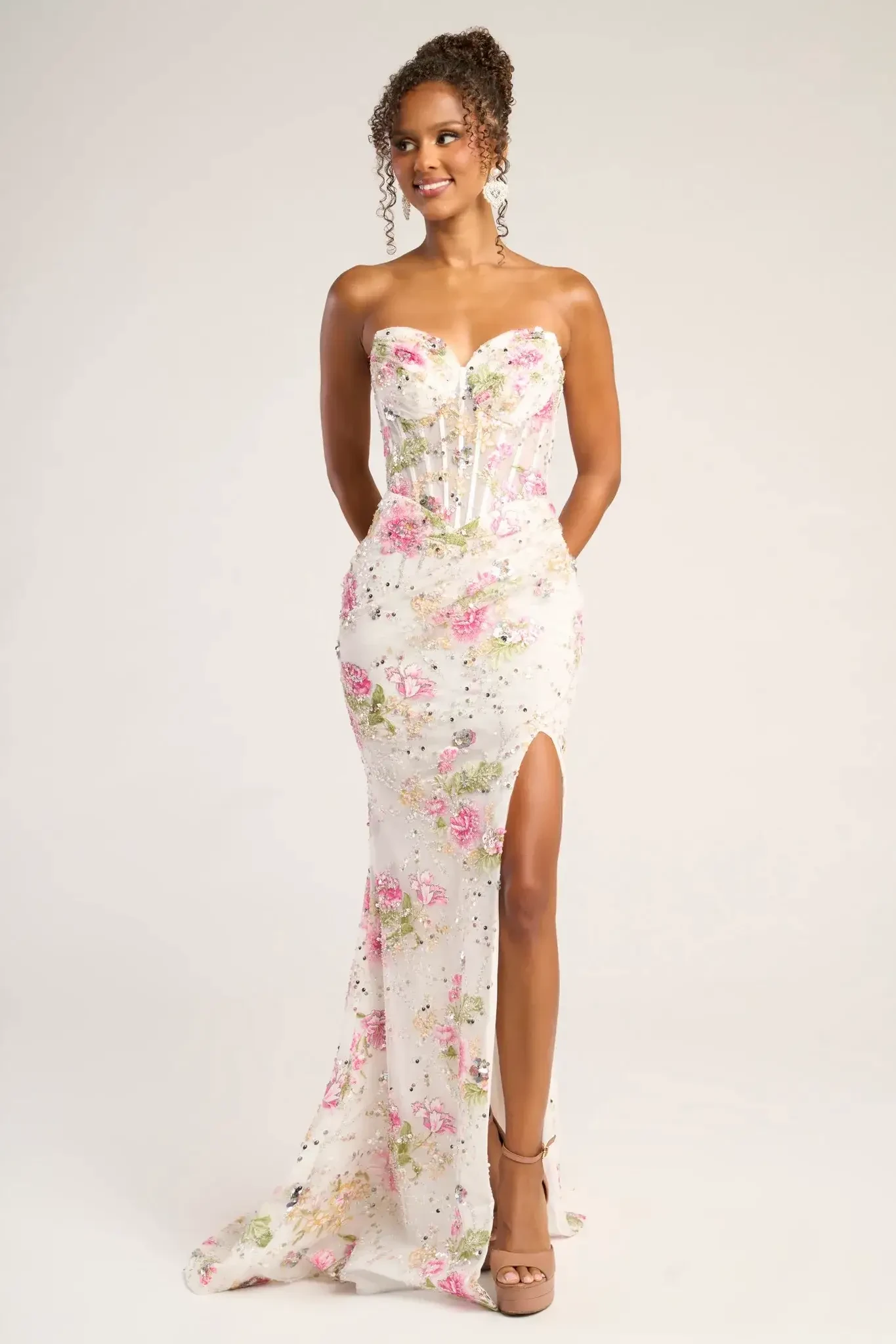 A woman in a floral strapless gown poses confidently, the dress featuring pink and green patterns with a high slit. The overall tone is elegant and joyful.